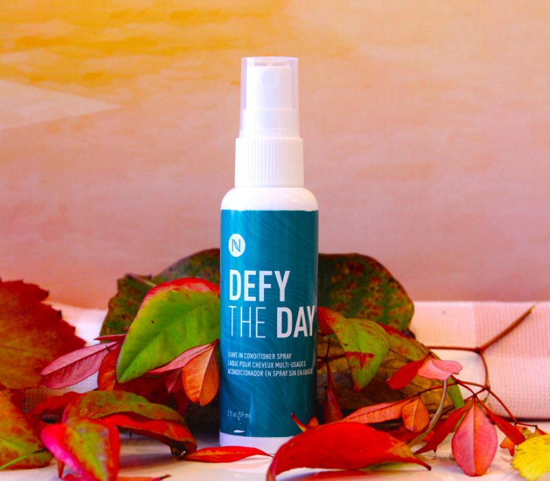 Neora's Defy the Day Leave-In Conditioner sitting in a bed of spring flowers.